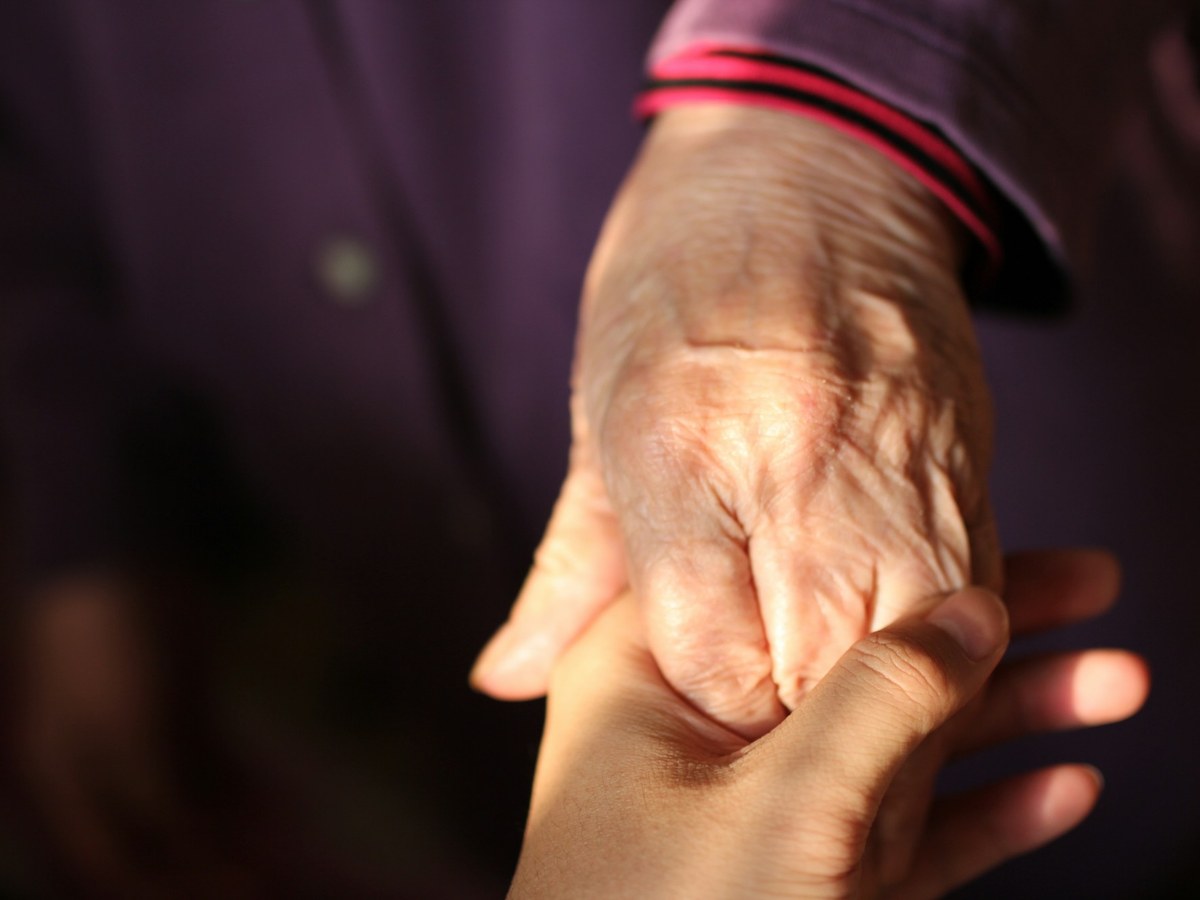 Mano de un adulto mayor sostenida por una mano joven
